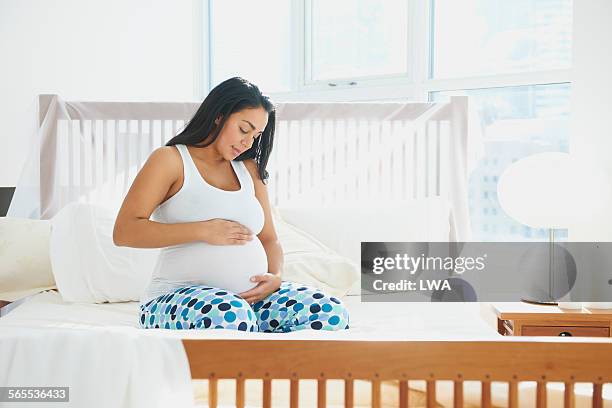 pregnant woman holding her stomach in bed - black pants stock pictures, royalty-free photos & images