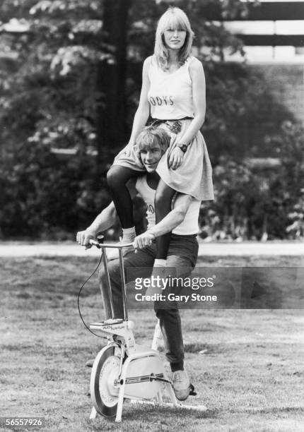 English racing driver James Hunt poses on an exercise bicycle with ex-girlfriend Jane Birbeck on his shoulders to publicise the opening of their...