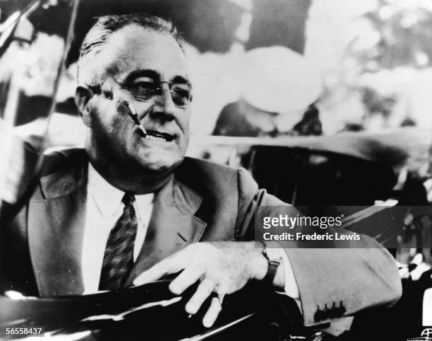 American President Franklin Delano Roosevelt , 32nd President of the United States, smokes a cigarette and sits in the driver's seat of a convertible...