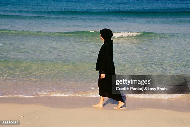 a woman seen strolling near the seashore. - muslim woman beach stock-fotos und bilder