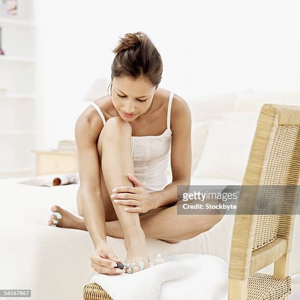 young woman sitting on the floor painting her toenails - painting toenails stock-fotos und bilder