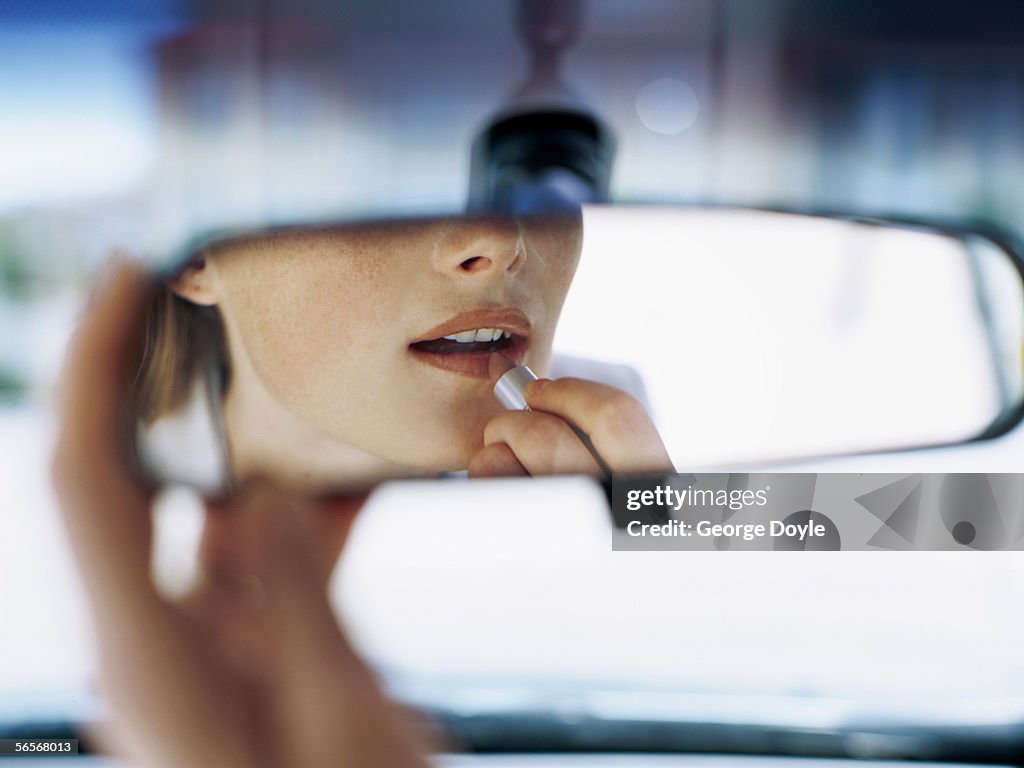 Young woman applying lipstick in a car