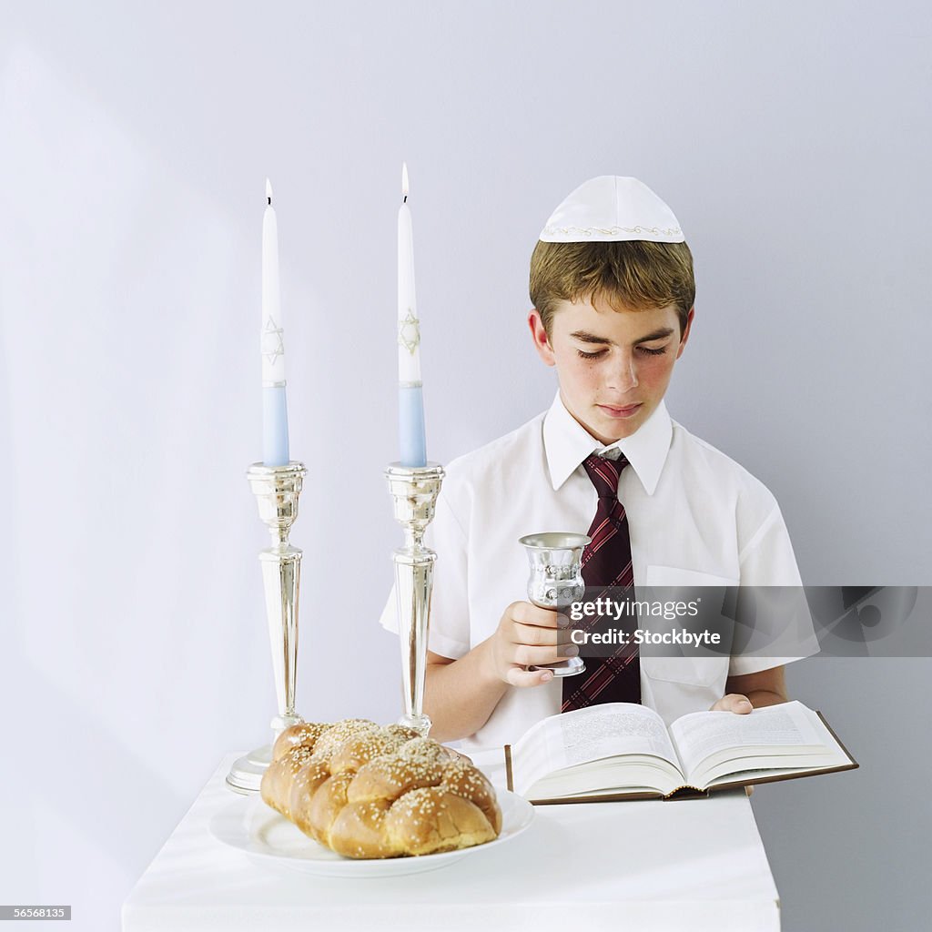 Jewish boy reading the talmud with a Kiddush cup in hand