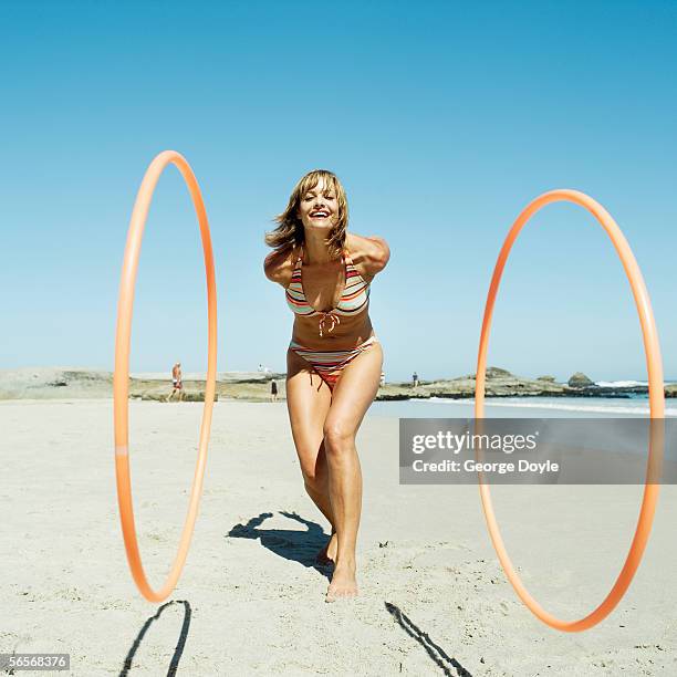 portrait of a young woman rolling hoops on the beach - hoop rolling stock pictures, royalty-free photos & images