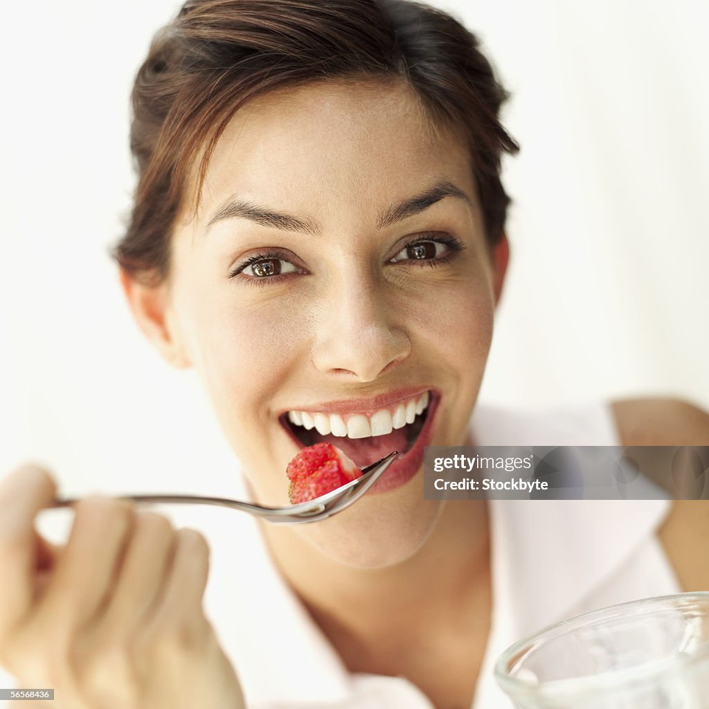 Portrait of a young woman eating a strawberry with a spoon