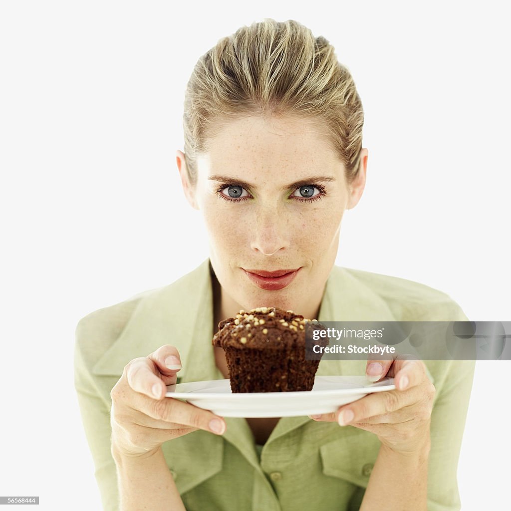 Portrait of a young woman holding a muffin on a plate