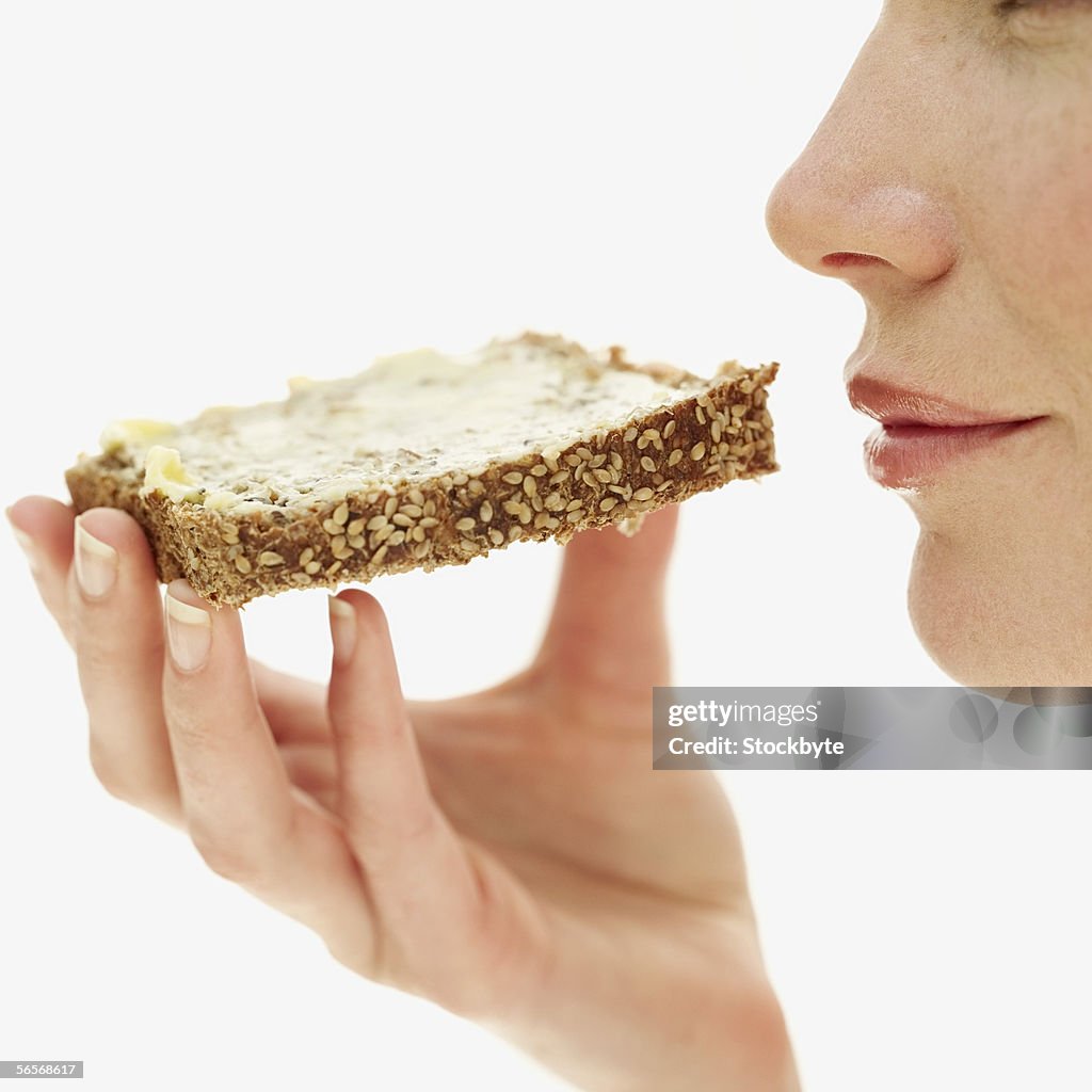 Side profile of a young woman holding a piece of sesame seed toast