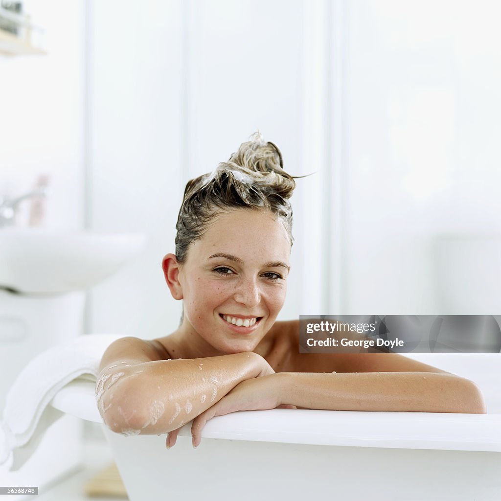 Portrait of a young woman sitting in a bathtub with shampoo in her hair