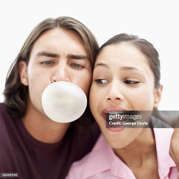 close-up of a young woman looking at a young man blowing a chewing gum bubble - masticar fotografías e imágenes de stock