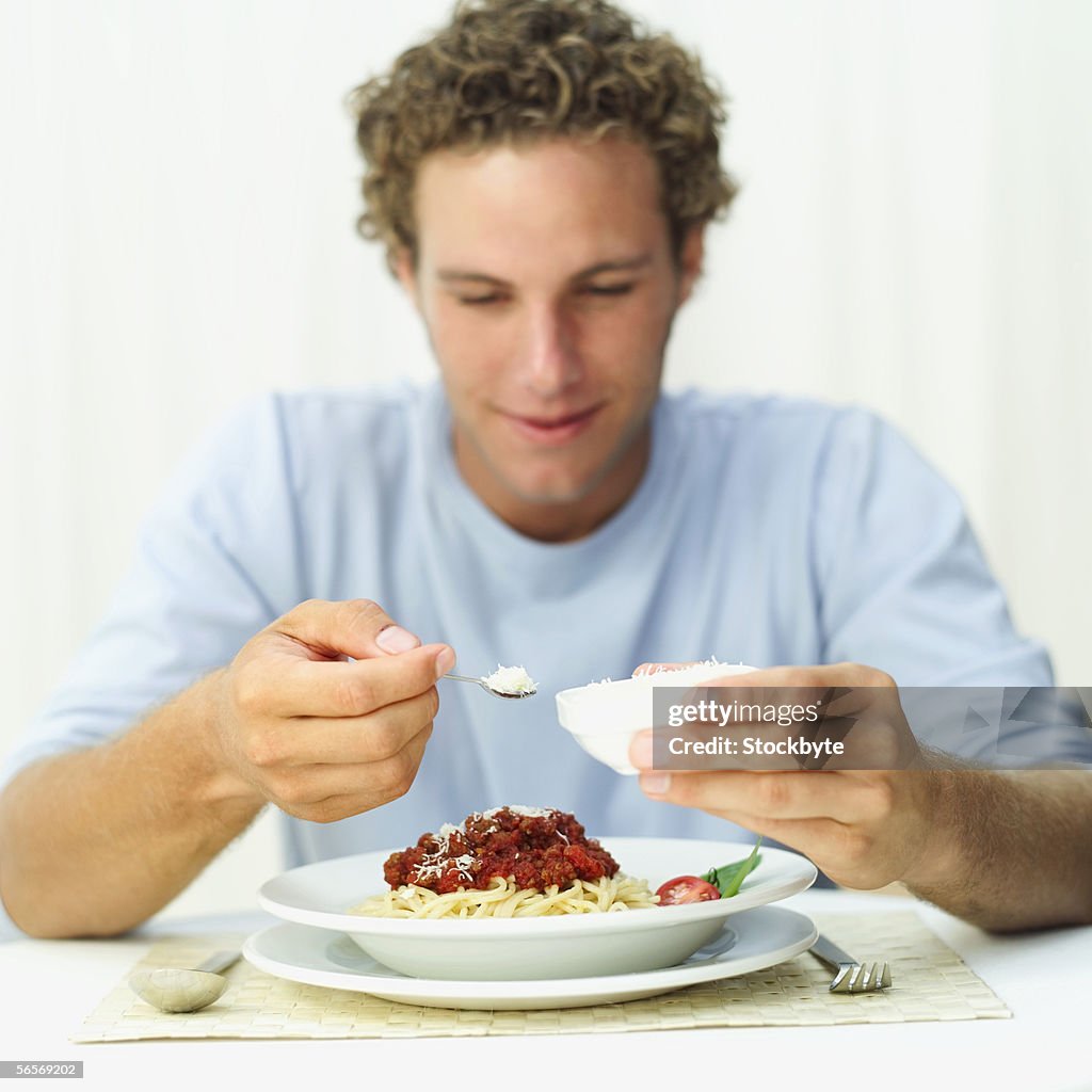 Young man sprinkling grated cheese onto spaghetti in a bowl