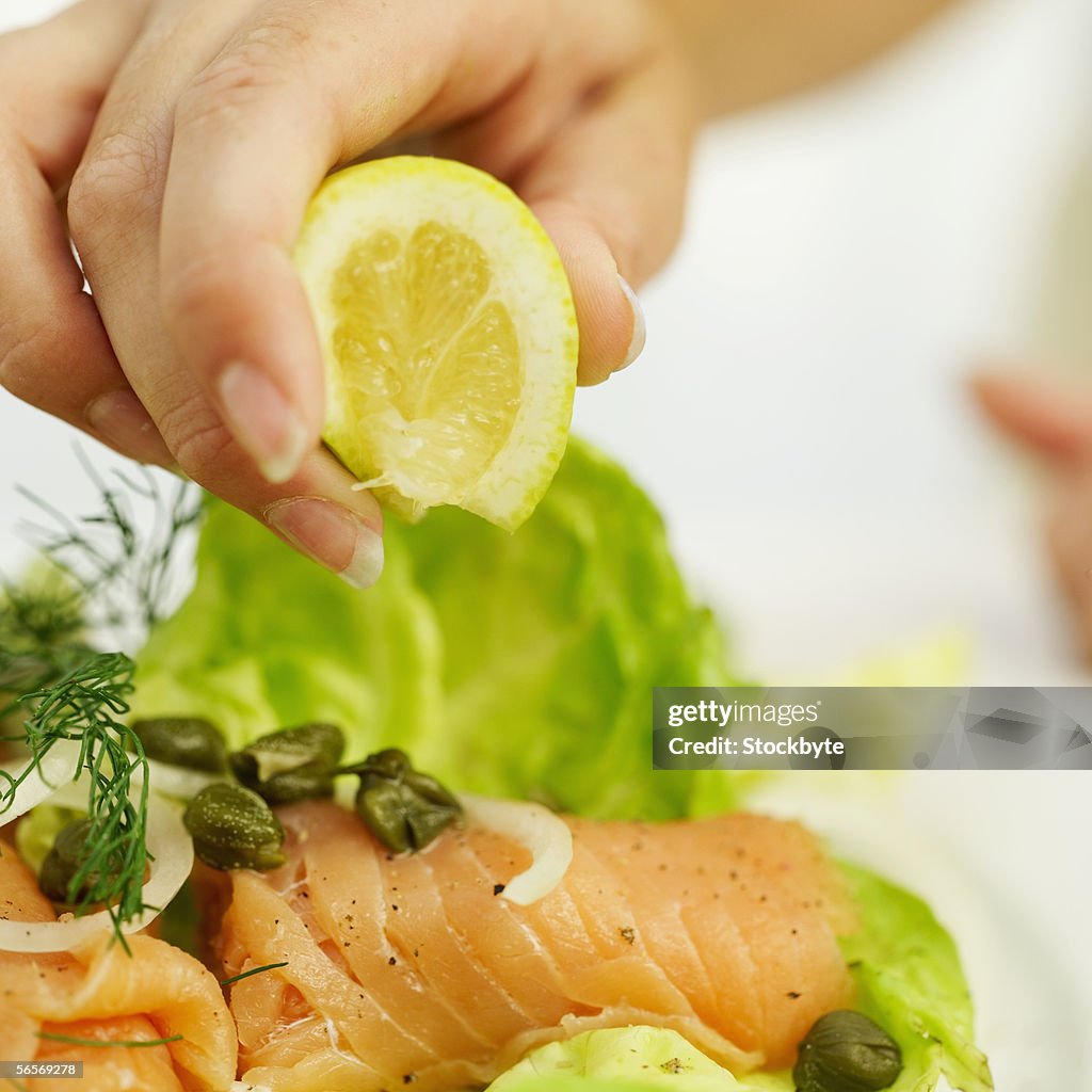 Close-up of a person's hand squeezing lemon on a sushi salad