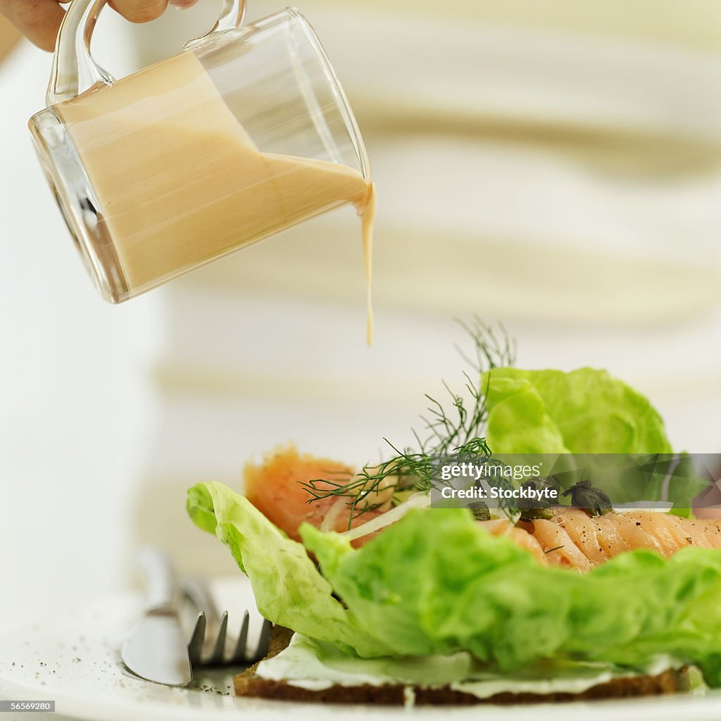 Close-up of a person's hand pouring a jug of salad dressing over a sushi salad