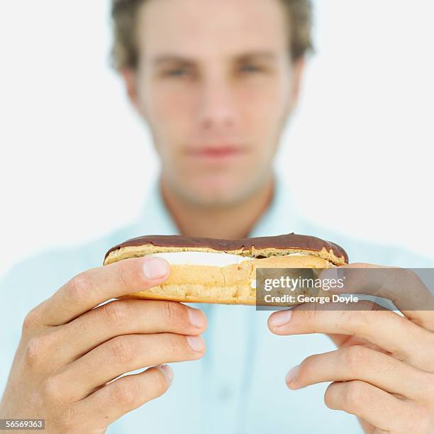close-up of a chocolate eclair in a young man's hands - eclair stock pictures, royalty-free photos & images