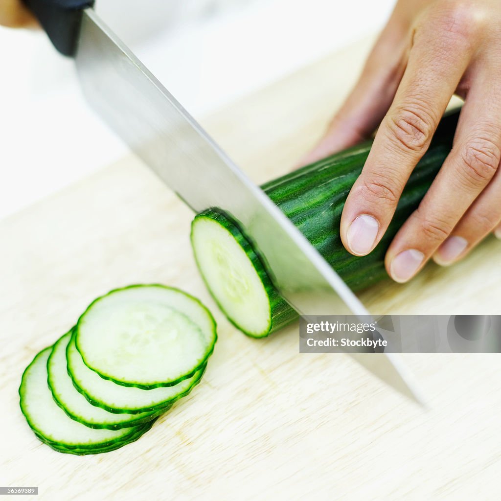 High angle view of a person's hand slicing a cucumber with a knife