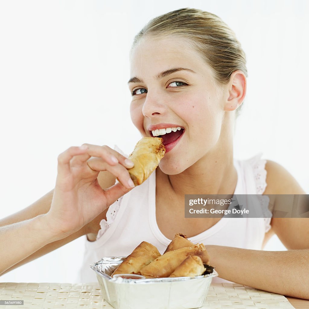 Teenage girl eating a spring roll from a box