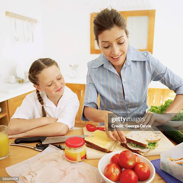 young mother making a ham sandwich with a young girl (8-10) watching her - een broodje smeren stockfoto's en -beelden