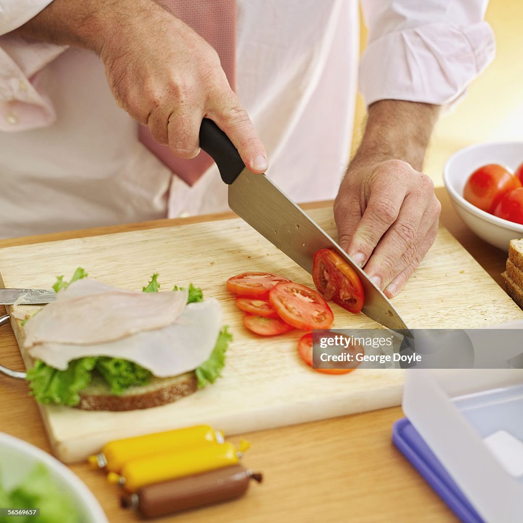 Mid section view of a man slicing a tomato on a cutting board