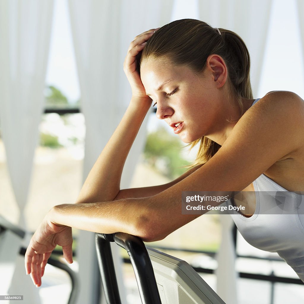 Side profile of a young woman resting on the handlebars of an exercise bike