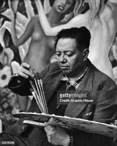 Mexican painter Diego Rivera selects a brush from his palette while he works on a mural, 1948.