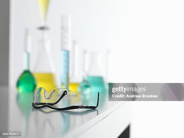 safety glasses on laboratory bench with a chemical experiment in background - lab bench stock pictures, royalty-free photos & images