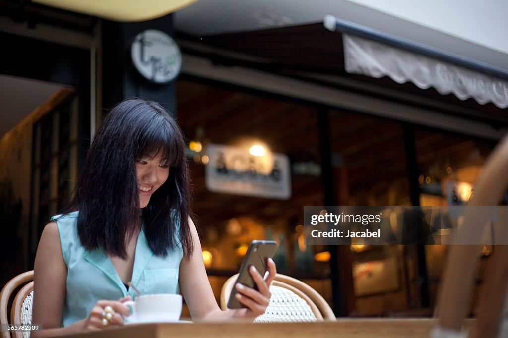 Young woman, sitting outside cafe, using smartphone, Shanghai, China
