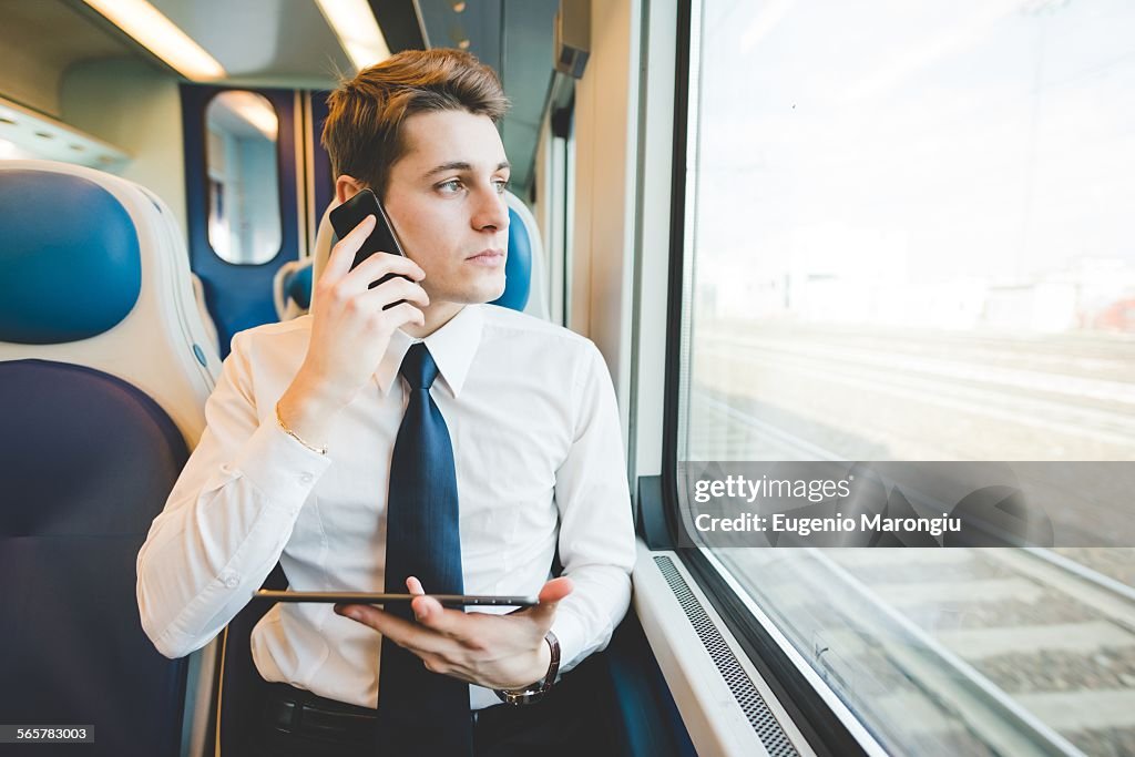 Portrait of young businessman commuter using digital tablet on train.