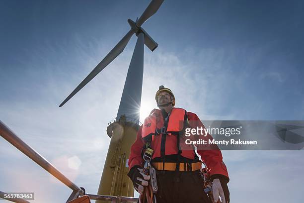 engineer preparing to climb windturbine at offshore windfarm, low angle view - offshore windfarm stock pictures, royalty-free photos & images