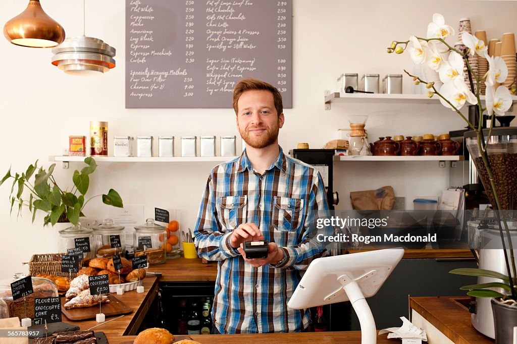 Portrait of cafe waiter with card machine behind counter