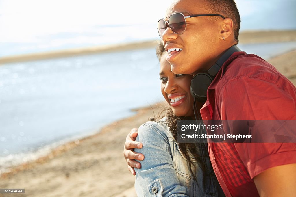 Young couple standing together on beach smiling, hugging looking away