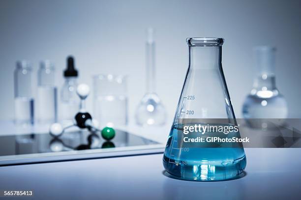 chemistry research. erlenmeyer flask containing colored liquid and a digital tablet with a ball-and-stick molecular model on its screen - bouteille d'erlenmeyer photos et images de collection