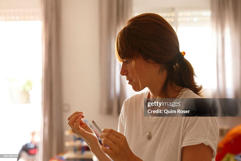 Mid adult woman at home using nail file