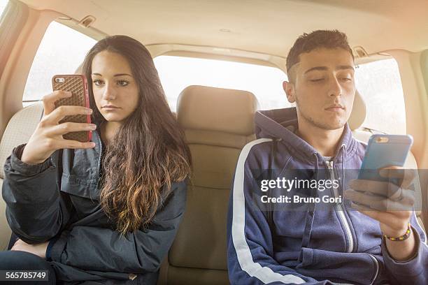 teenage girl and young man reading separate smartphone texts in car back seat - teens brothers stock-fotos und bilder