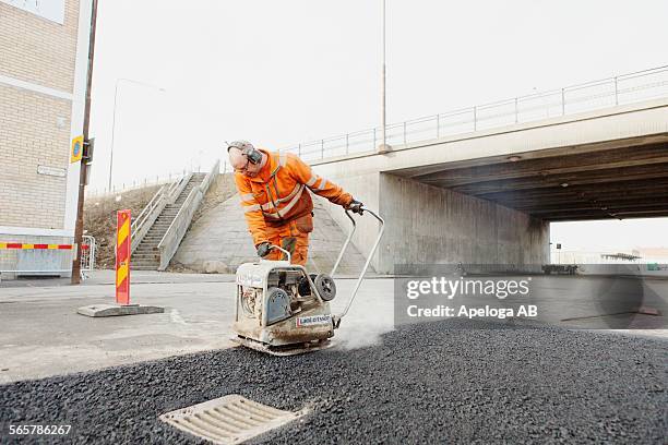 mature manual worker laying asphalt at road construction site - voie urbaine photos et images de collection