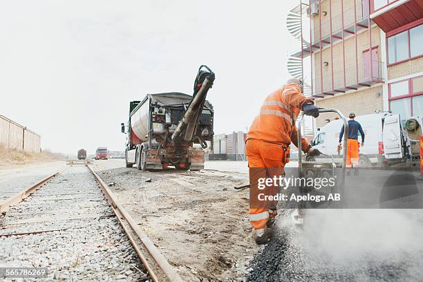 rear view of manual worker laying asphalt at construction site - tejer stock-fotos und bilder