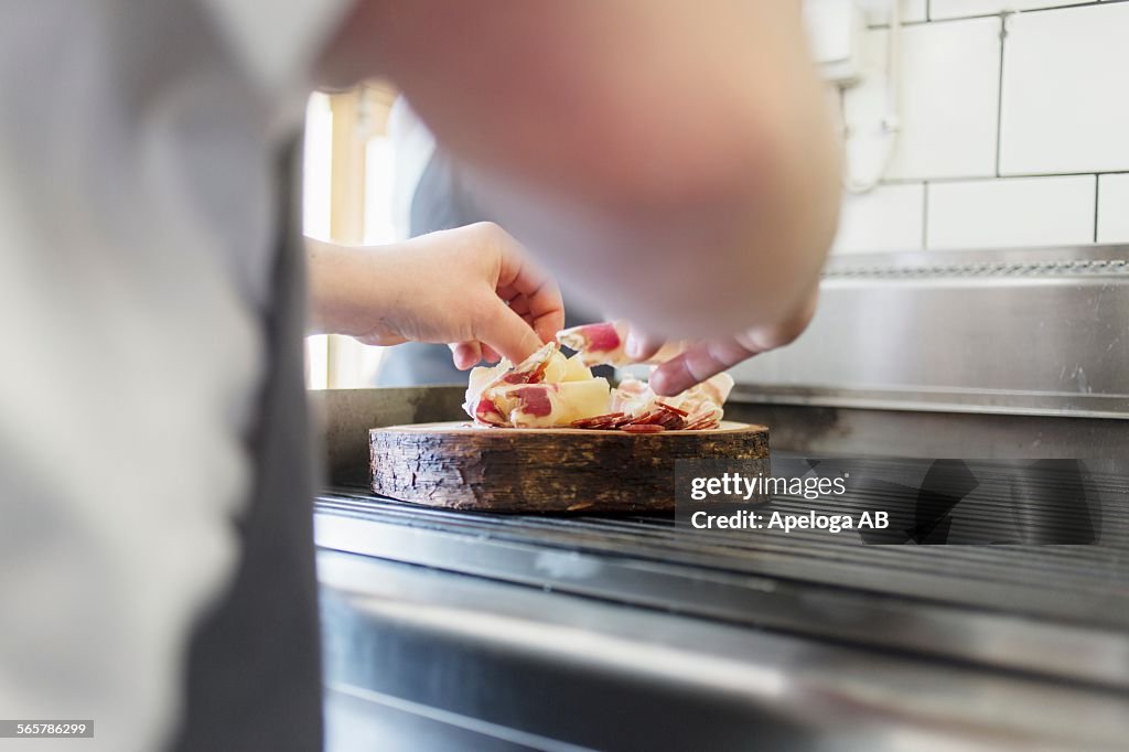 Cropped image of chef arranging meat slices on wooden plate in kitchen