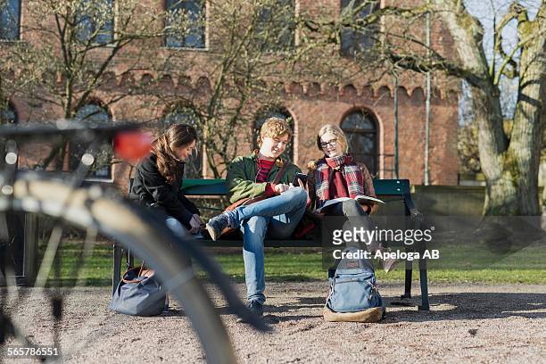teenage friends with books and mobile phone sitting on bench in campus - 3 teenagers mobile outdoors stock-fotos und bilder