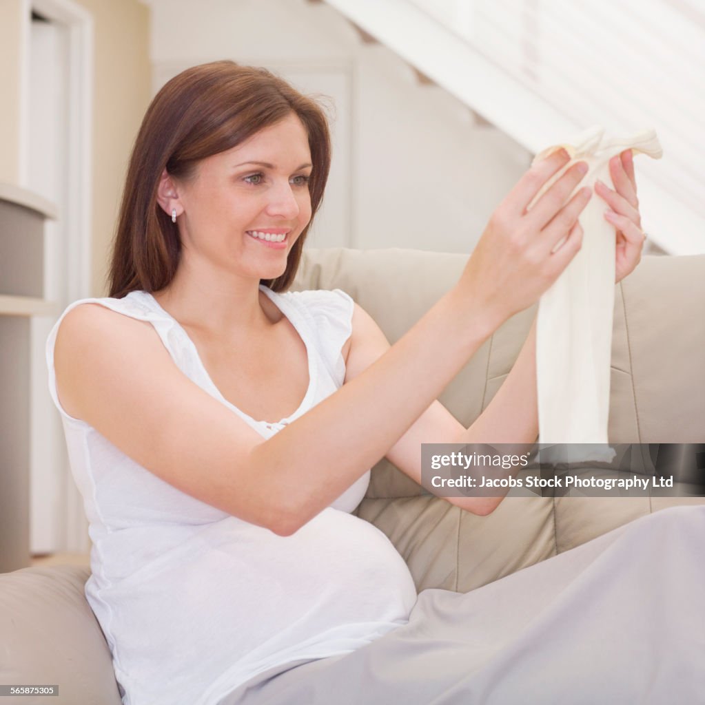 Pregnant Caucasian woman admiring baby clothes