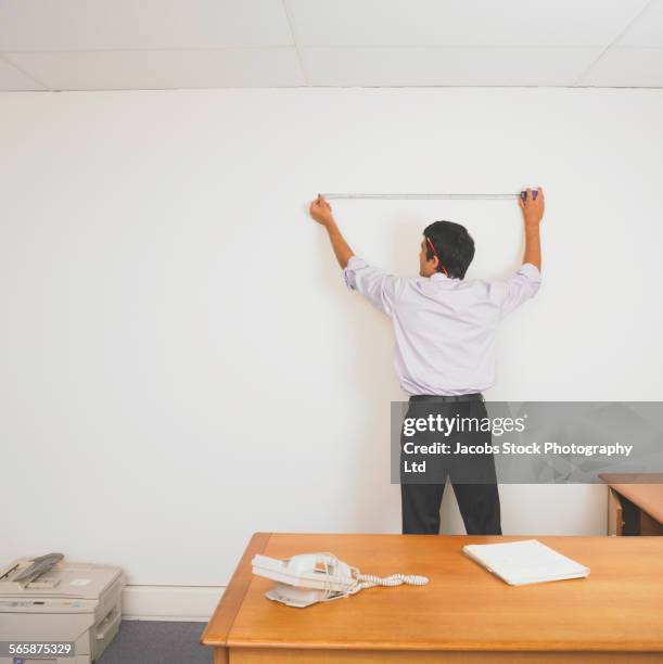 hispanic businessman using tape measure to measure wall - measuring potential business stock pictures, royalty-free photos & images