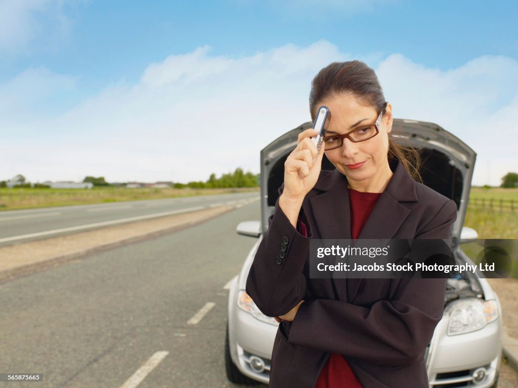Caucasian businesswoman with broken-down car on rural road