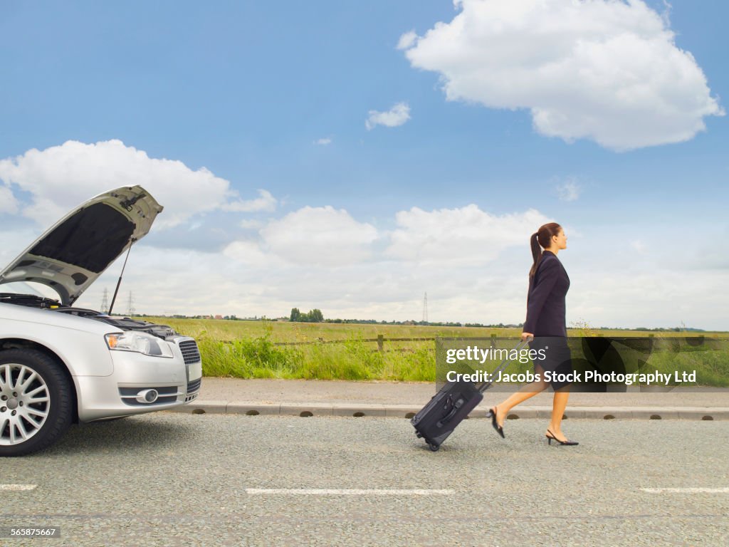 Caucasian businesswoman leaving broken down car on rural road