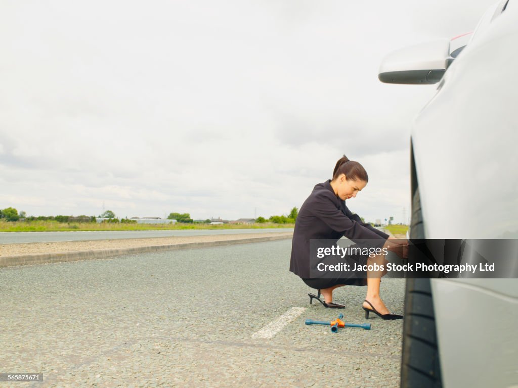 Caucasian businesswoman changing car tire on rural road