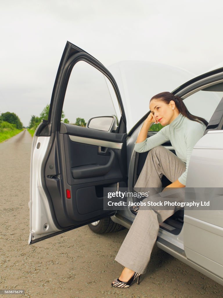Caucasian businesswoman in broken down car on rural road