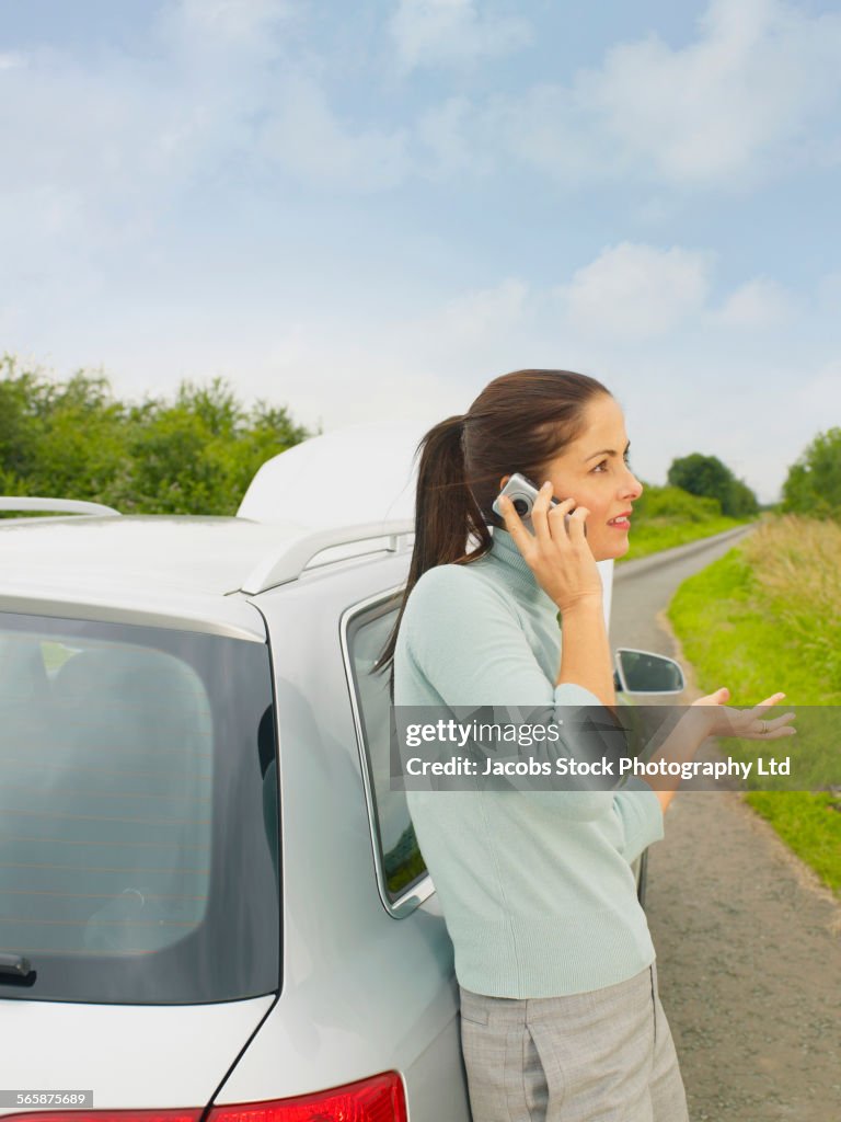Caucasian businesswoman calling for help from broken down car on rural road