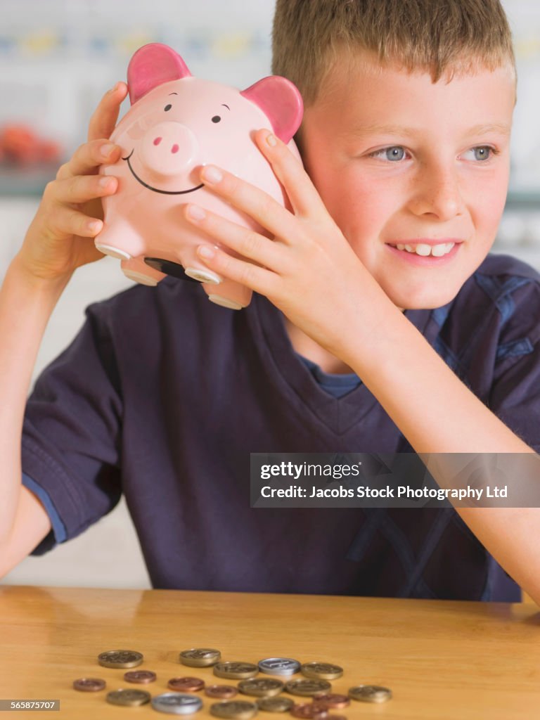 Caucasian boy shaking coins in piggy bank