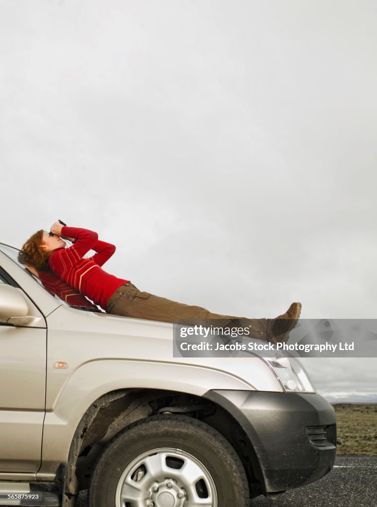 Caucasian woman admiring sky with binoculars on car