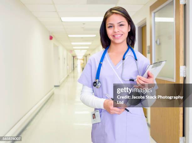 hispanic nurse carrying clipboard in hospital hallway - entry draft portraits stock pictures, royalty-free photos & images