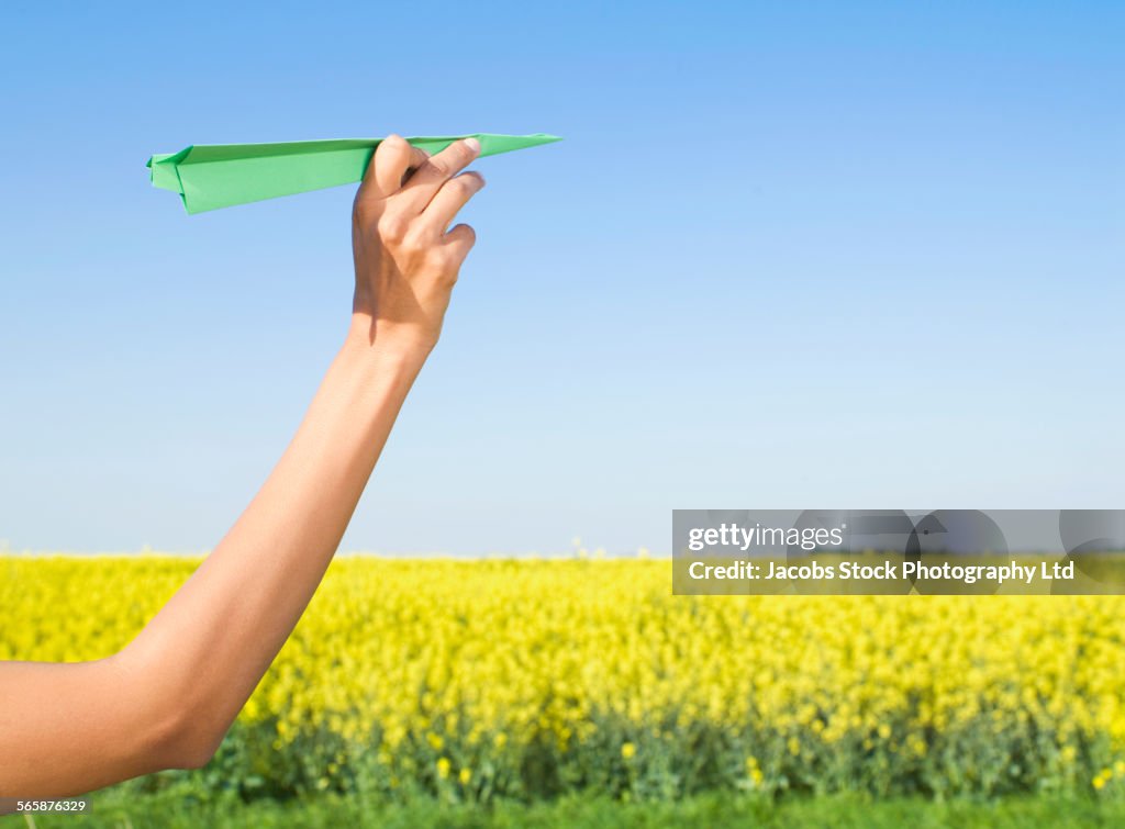 Indian woman holding green paper airplane in field of flowers