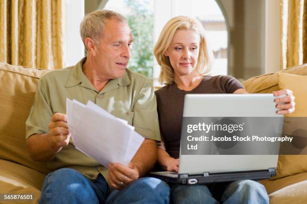 caucasian couple paying bills with laptop on sofa - surprise arizona stockfoto's en -beelden