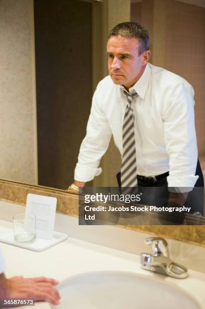 upset caucasian businessman staring in hotel bathroom mirror - skjorta och slips bildbanksfoton och bilder