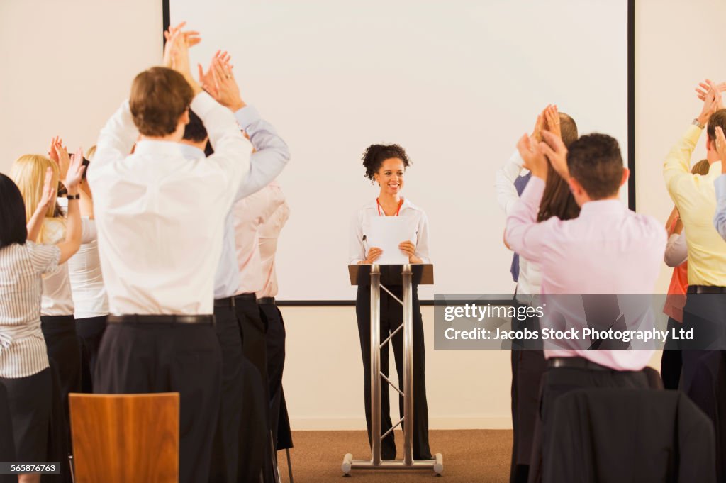 Audience applauding businesswoman at podium